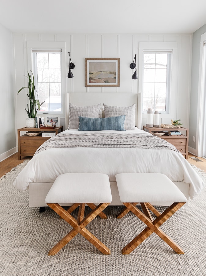 white walls, coastal wall art. white bed with windows on either side. Blue and gray bedding. Coastal bedroom design