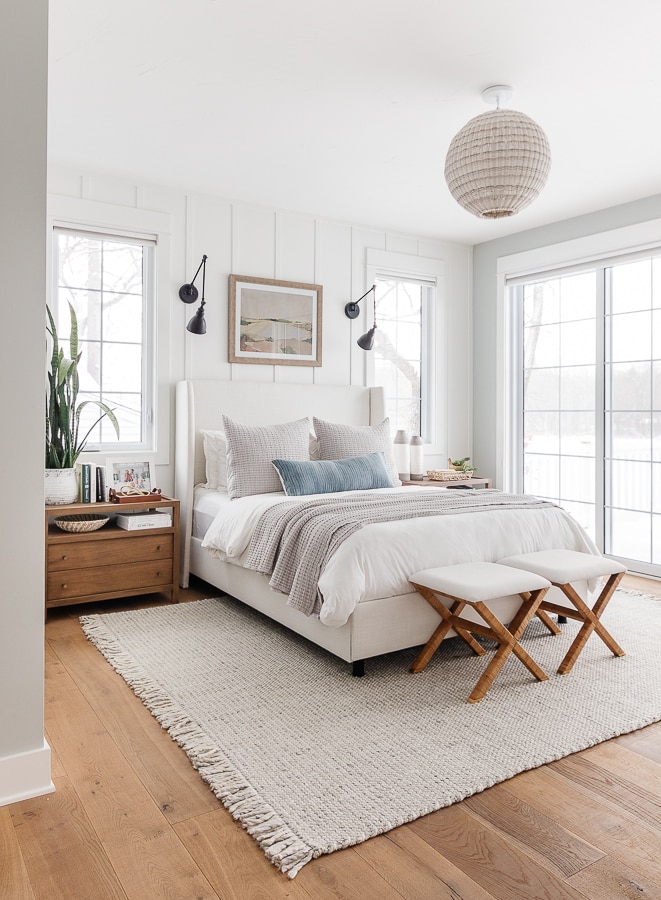 white paneled walls with blue paint. White bedding with gray rug and throw pillows. Coastal bedroom decor