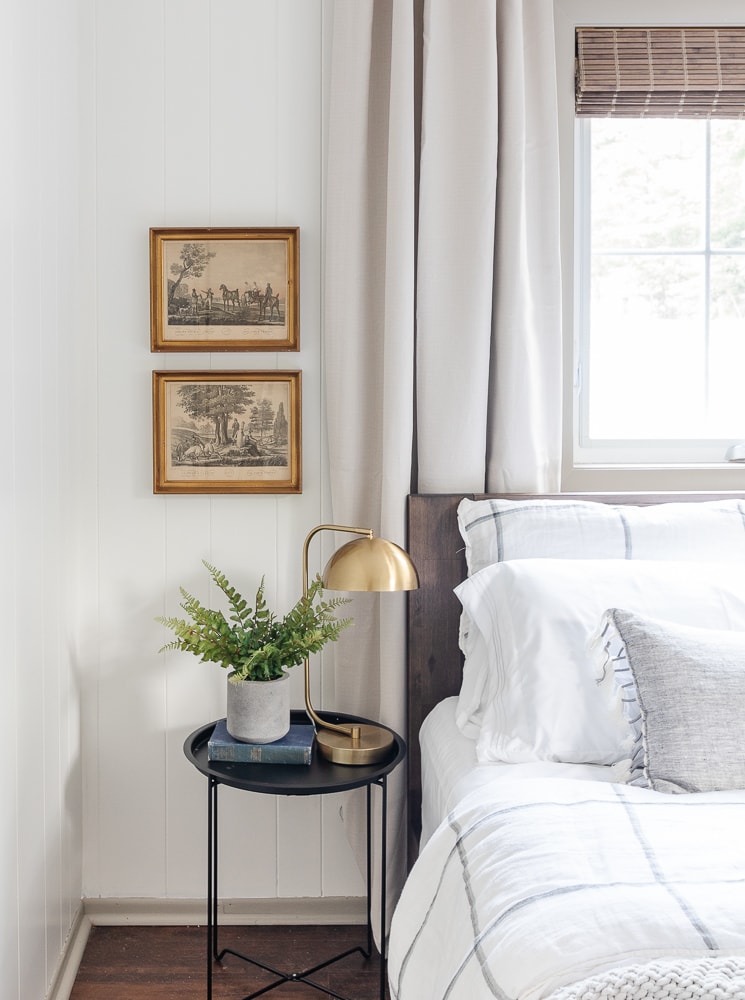 neutral bedroom, black end table, brass lamp, white and gray bedding