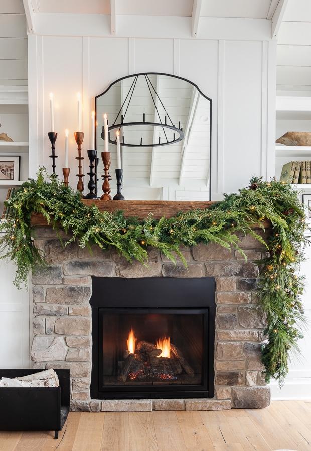White living room with stone fireplace with Christmas decor. Black mirror and faux greenery 