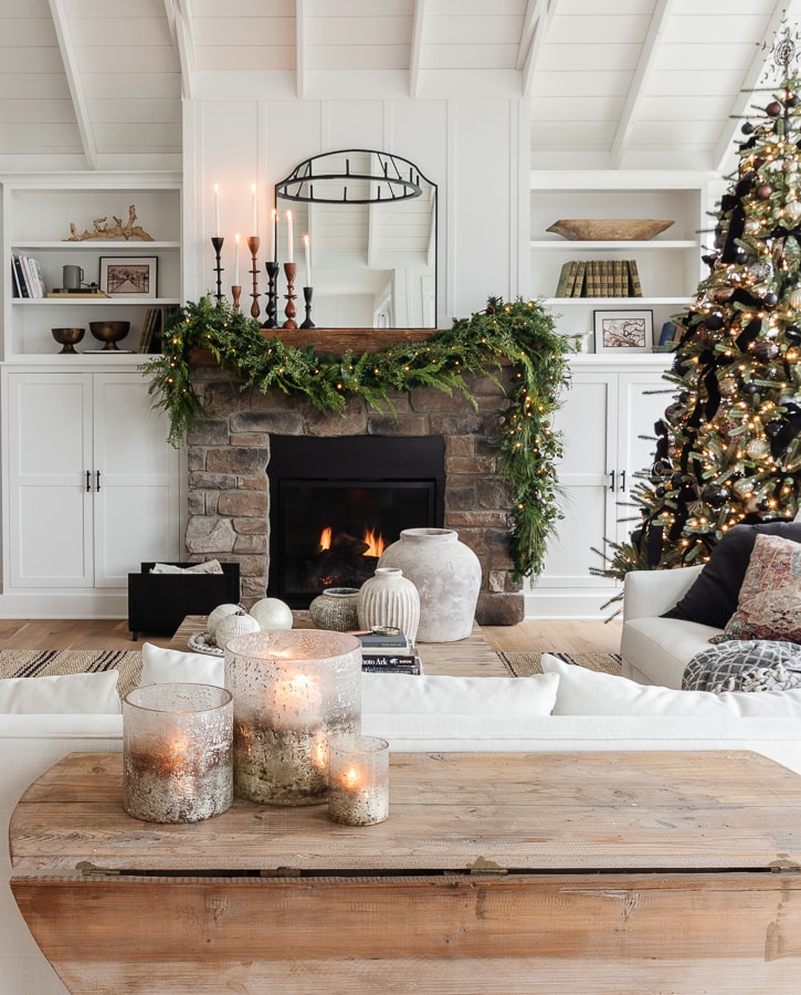 White living room with stone fireplace with black mirror and faux garland Christmas decor