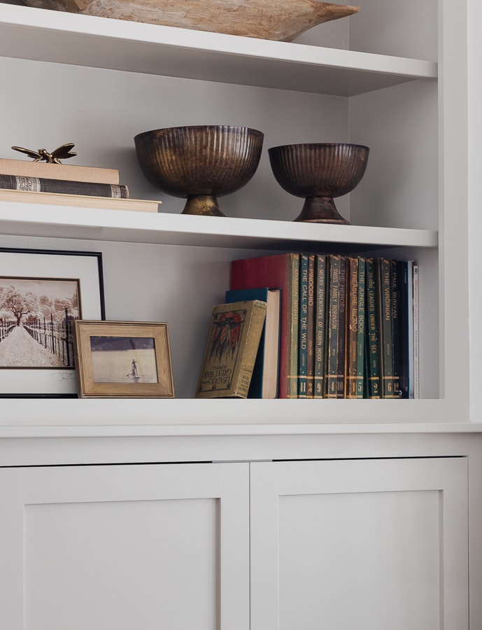 Gray bookshelves with vintage books and antique brass bowls