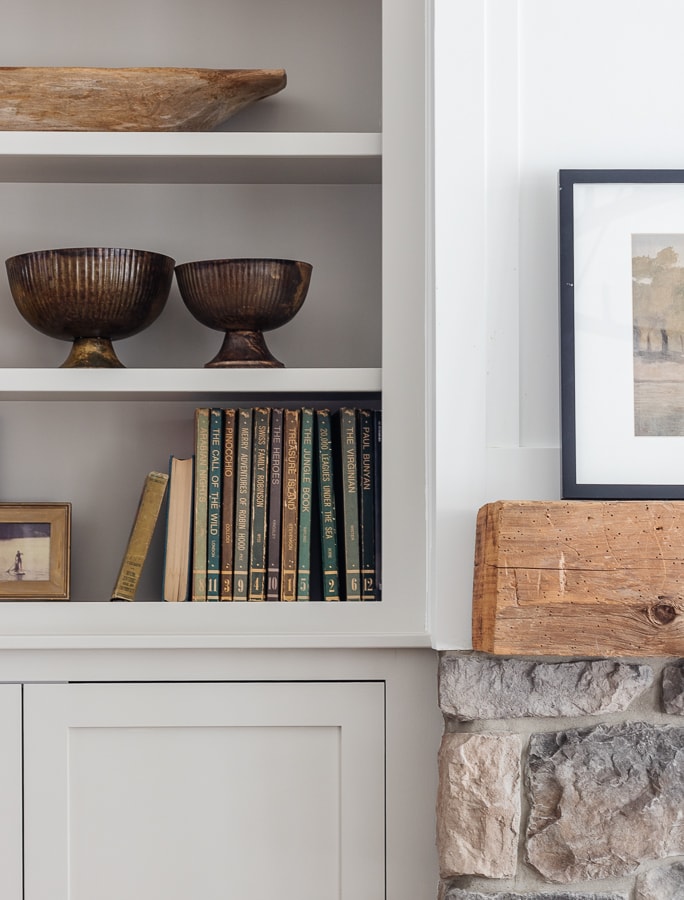 Gray bookshelves with vintage books and brass bowls next to a stone fireplace