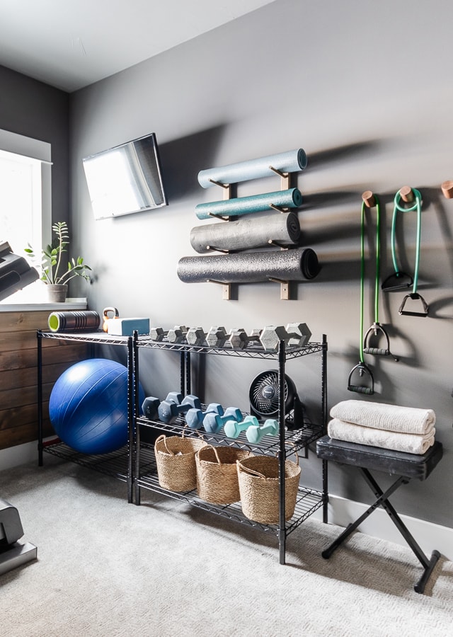 Dark gray gym wall with racks of weights and yoga mat racks