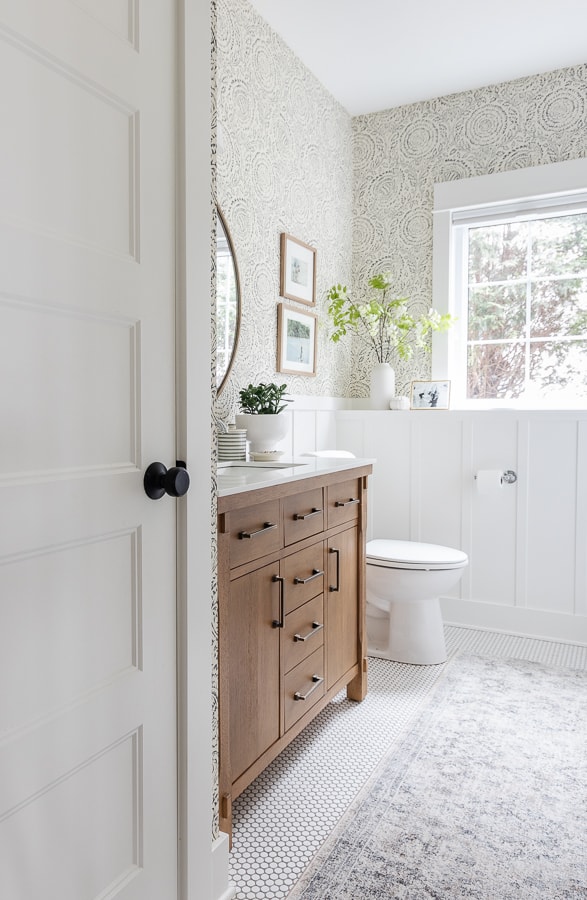 white bathroom with penny tile and wallpaper with wood vanity