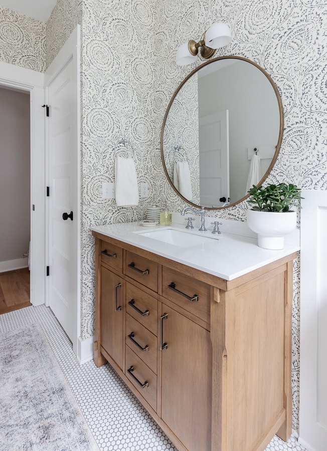 white bathroom with penny tile and wallpaper with wood vanity