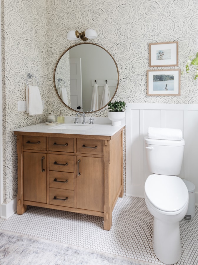 white bathroom with penny tile and wallpaper with wood vanity