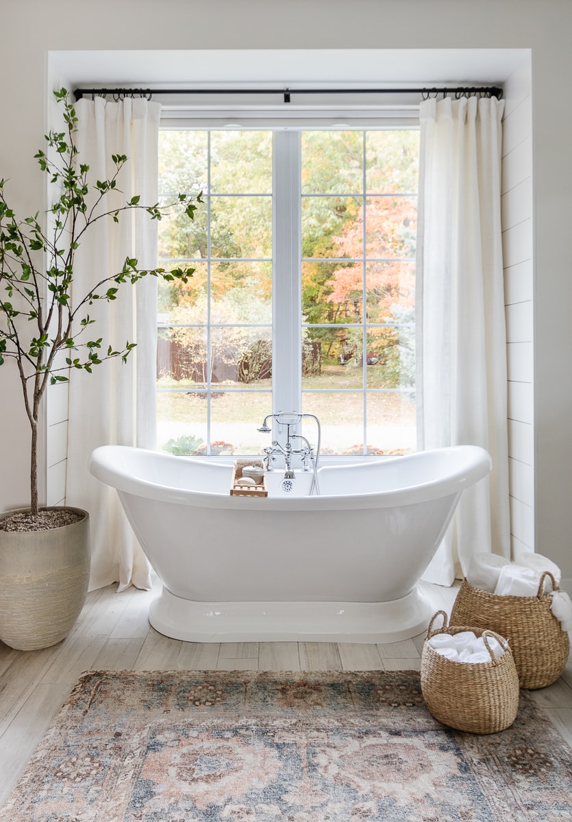 freestanding tub in front of large window with faux tree