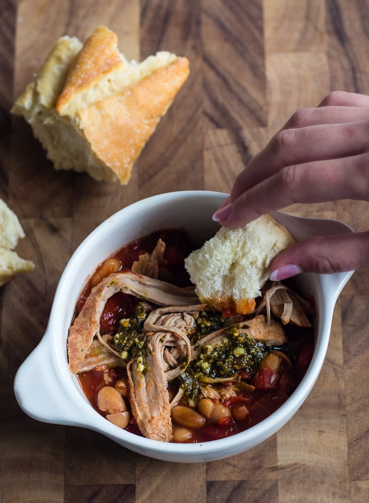 white bowl with pork and beans and crusty bread dipping in it