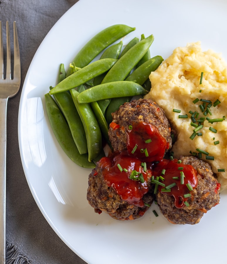 Meatloaf Meatballs on a white plate with mashed potatoes and peas