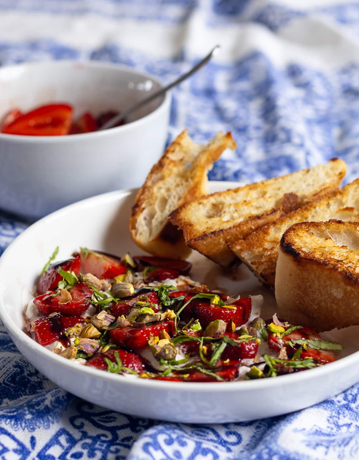 white bowl with burrata and strawberries with toasted bread